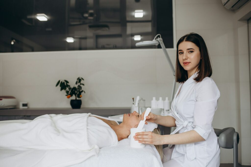 Woman beautician makes a face massage to patient in bathrobe